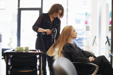 Friseurin trocknet langes Haar einer Kundin im Salon - CAIF14105