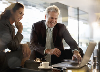 Smiling businessman and businesswoman using laptop in lobby - CAIF14202