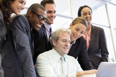 Lächelnde Geschäftsleute teilen sich einen Laptop in einer Besprechung - CAIF14217