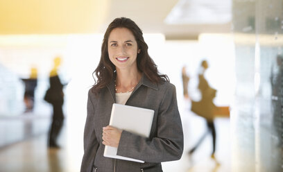 Portrait of smiling businesswoman holding digital tablet in lobby - CAIF14231