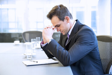 Businessman with head in hands in conference room - CAIF14250