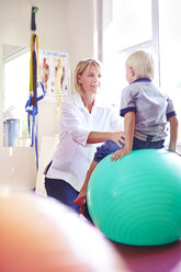 Physiotherapeutin hält Jungen auf Fitnessball - CAIF14303