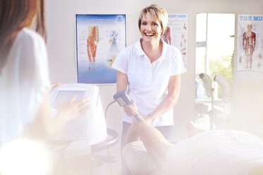 Lächelnde Physiotherapeutin mit Ultraschallsonde am Bein eines Patienten - CAIF14304