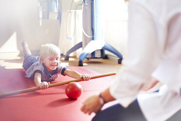 Physiotherapeutin führt Junge, der einen Ball mit einem Stock rollt - CAIF14313