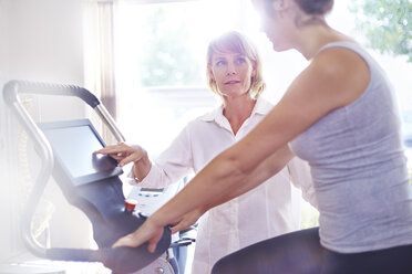 Physical therapy guiding woman on stationary bike - CAIF14328