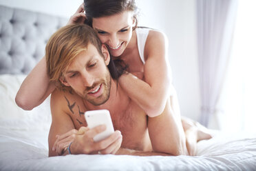 Couple laying on bed texting with cell phone - CAIF14388