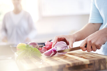 Woman slicing red onion on cutting board in kitchen - CAIF14420