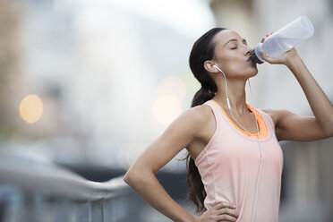 Woman drinking water after exercising on city street - CAIF14521