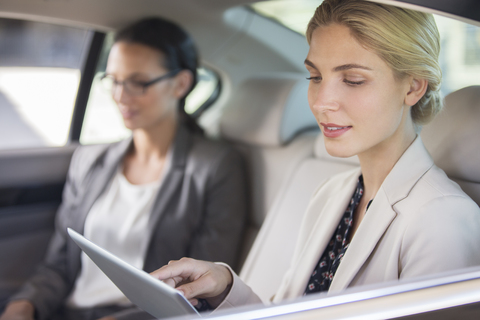 Geschäftsfrau mit digitalem Tablet auf dem Rücksitz eines Autos, lizenzfreies Stockfoto