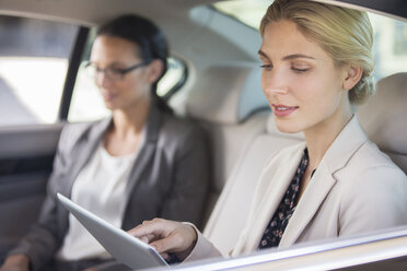 Businesswoman using digital tablet in car back seat - CAIF14532