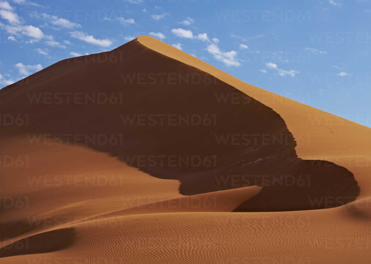 View of sand dunes in desert with blue sky and clouds in background stock  photo