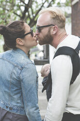 View of couple in sunglasses kissing and holding baby in city streets - CAIF14552