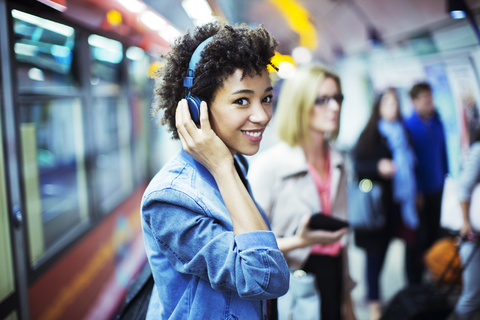 Lächelnde Frau hört in der U-Bahn Kopfhörer, lizenzfreies Stockfoto