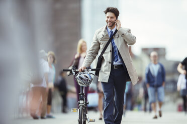 Businessman talking on cell phone pushing bicycle in city - CAIF14562