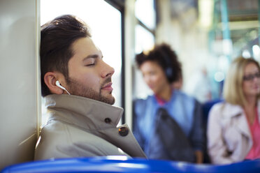 Businessman napping and listening to earbuds on train - CAIF14577