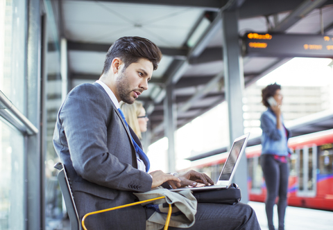 Businessman using laptop at train station stock photo