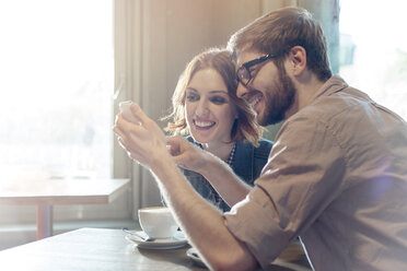 Couple using cell phone in sunny cafe - CAIF14617