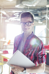 Portrait of casual businessman holding laptop in sunny office - CAIF14631