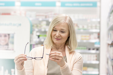 Customer looking at price tag on reading glasses in pharmacy - CAIF14664