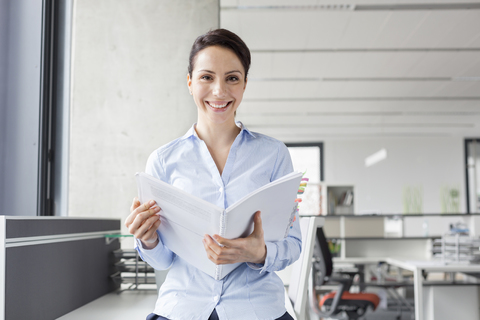 Porträt lächelnde Geschäftsfrau mit Bericht im Büro, lizenzfreies Stockfoto