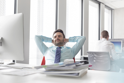 Entspannter Geschäftsmann, der mit den Händen hinter dem Kopf am Computer im Büro sitzt, lizenzfreies Stockfoto