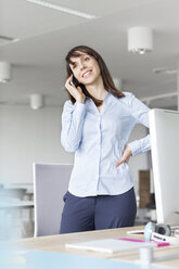 Brünette Geschäftsfrau im Gespräch am Handy am Schreibtisch im Büro - CAIF14778