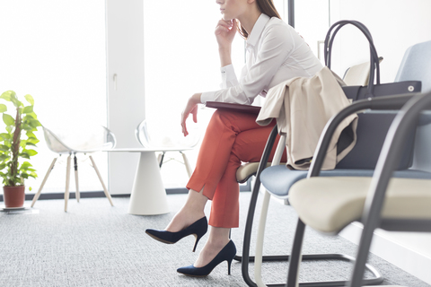 Geschäftsfrau wartet mit gekreuzten Beinen in der Lobby, lizenzfreies Stockfoto