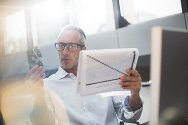 Businessman reading paperwork and cell phone in office - CAIF14805