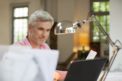 Älterer Mann benutzt Laptop im Heimbüro, lizenzfreies Stockfoto