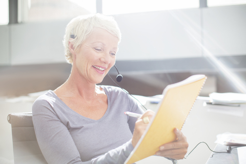 Geschäftsfrau mit Headset, die im Büro auf einen Notizblock schreibt, lizenzfreies Stockfoto