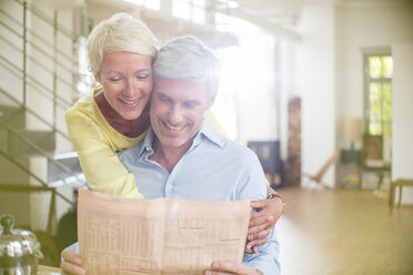 Older woman hugging husband reading newspaper - CAIF14851