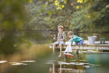Jungen angeln und spielen mit Spielzeug-Segelboot am See - CAIF15003