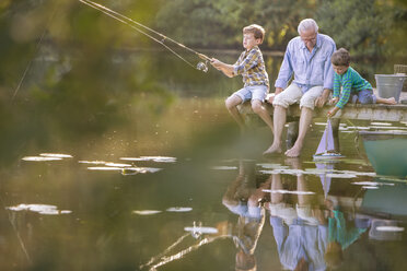 Grandfather and grandsons fishing and playing with toy sailboat at lake - CAIF15006