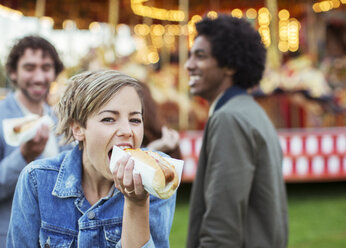 Three young people eating hot-dogs in amusement park - CAIF15018