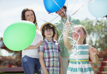 Junges Mädchen hält ein Bündel Luftballons, Familie steht hinter ihr - CAIF15026