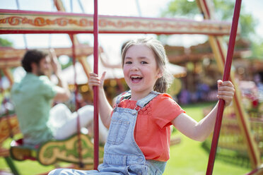 Cheerful girl laughing on carousel in amusement park - CAIF15042