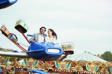 Couple enjoying ride on carousel in amusement park - CAIF15043
