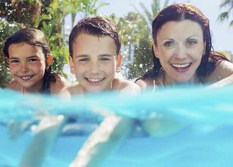 Porträt einer Mutter mit ihren beiden Kindern im Schwimmbad, lizenzfreies Stockfoto