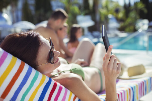 Frau beim Sonnenbaden und SMS schreiben am Swimmingpool - CAIF15071