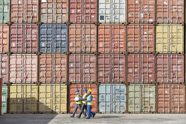 Arbeiter gehen zusammen in der Nähe eines Stapels von Frachtcontainern - CAIF15085
