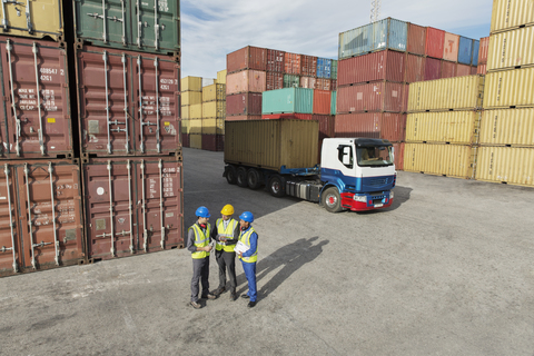 Geschäftsleute und Arbeiter unterhalten sich in der Nähe von Frachtcontainern, lizenzfreies Stockfoto