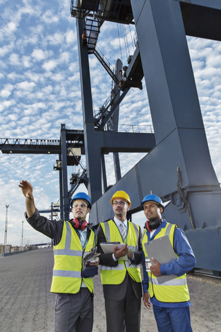 Geschäftsleute und Arbeiter unterhalten sich in der Nähe eines Frachtkrans, lizenzfreies Stockfoto