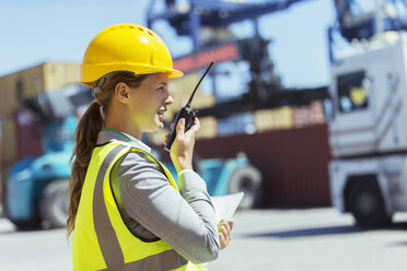 Businesswoman using walkie-talkie near cargo containers and trucks - CAIF15137