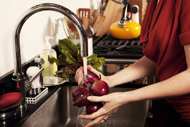 Mittelteil einer Frau beim Waschen von Roter Bete in der Küche - CAVF06080