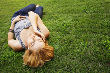 Woman listening music while lying on grassy field at park - CAVF06086