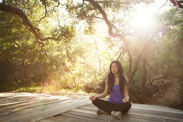 Woman meditating while sitting in forest - CAVF06096