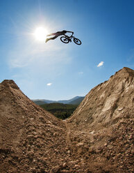 Silhouette of man with bicycle jumping on mountain against sky - CAVF06161