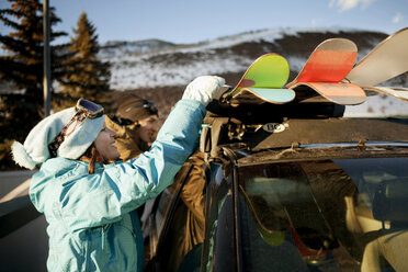 Side view of woman removing skis from car while standing by friend at ski resort - CAVF06179