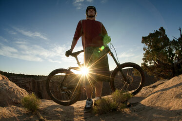 Niedriger Blickwinkel auf einen Mann mit Fahrrad, der auf einem Berg gegen den Himmel steht - CAVF06186