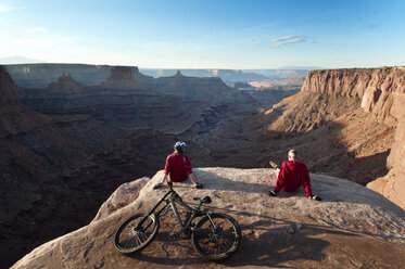 Rückansicht von Mountainbikern, die sich auf einer Klippe vor dem Himmel entspannen - CAVF06205